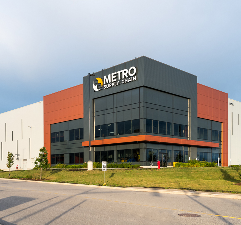 A side view of a building with a logo branded logo on top that say Metro Supply Chain